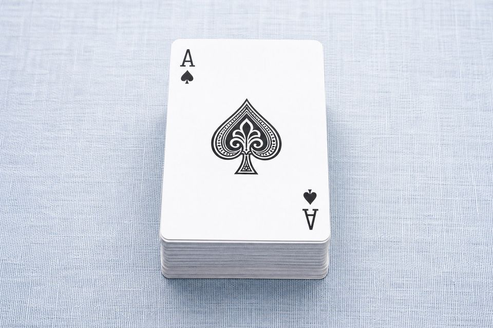 浅蓝亚麻桌布上整齐叠放的一副扑克牌,最上方是黑桃A